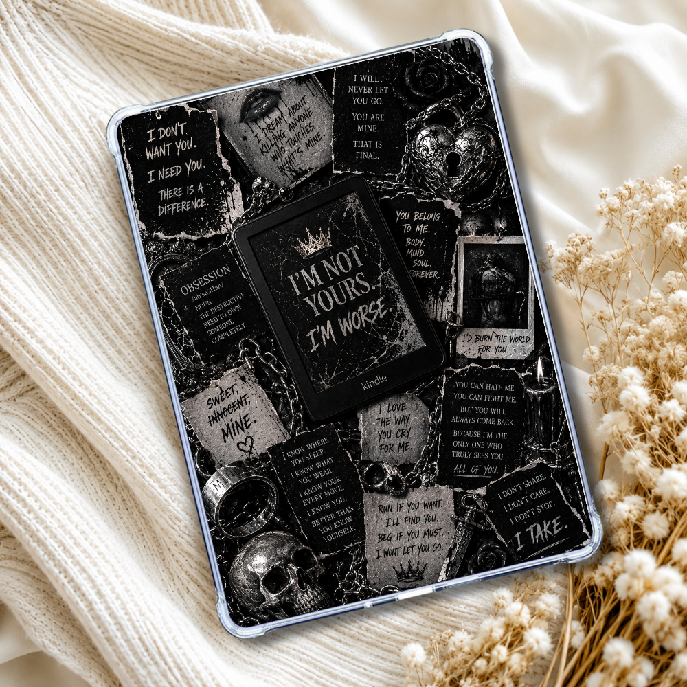 A tablet case with a gothic collage print featuring skulls, chains, and text like 'I'M NOT YOURS I'M WORSE' and 'I TAKE', shown on a phone. The case is styled on a cream knit blanket with dried flowers.