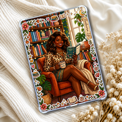 A clear iPad case featuring a colorful illustration of a woman in a leopard-print top sitting in an orange armchair and reading a book, surrounded by bookshelves, plants, and decorative motifs. The case is styled on a cream knit blanket with dried flowers.