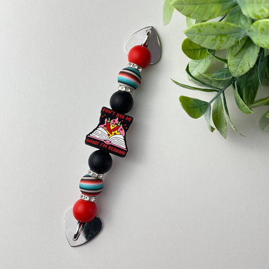 Decorative keychain with beads and a tag on a white surface with a plant in the background